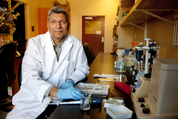 Dr. Bhide sits in front of lab bench.