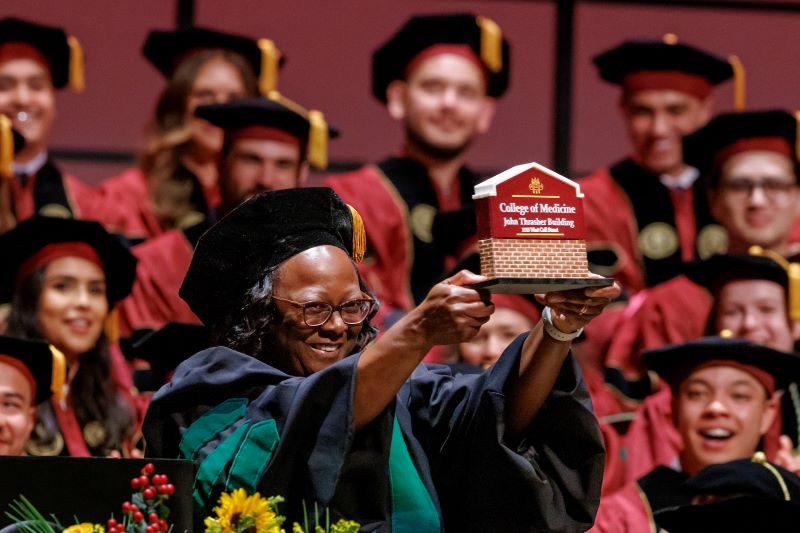 Dr. Alma Littles displays the replica of the College of Medicine sign created by the FSU Master Craftsmen Studio for the college to give President Emeritus John Thrasher, for whom the building is named.
