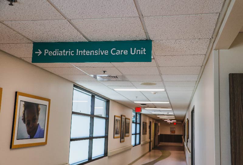 A sign in the hospital hall way pointing to the Pediatric Intensive Care Unit.