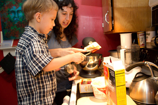 Adult supervises boy cooking.