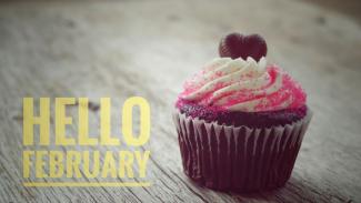 Chocolate cupcake with white frosting, pink sprinkles, and a chocolate heart sitting on a piece of wood. The caption says 
