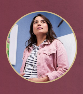 A woman with long dark hair wearing a pink denim jacket over a striped shirt, framed within a gold circular border.