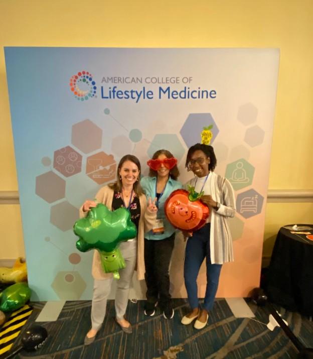 Three female residents holding balloons and posing in front of an American College of Lifestyle Medicine banner